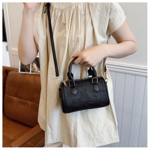 Model wearing black embossed mini handbag with bunny and bear patterns and gold hardware