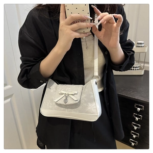 Nahaufnahme der weißen Schultertasche mit floraler Textur, Schleife und Herzanhänger