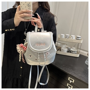 Detail of silver mini backpack featuring BCM3 embroidery and plush monkey charm accessory