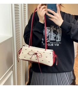 Détail du sac à bandoulière crème avec motifs nœuds rouges et pendentif cœur en métal