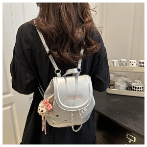 Détail d'un mini sac à dos argenté avec broderie IBCMB et charm de singe en peluche