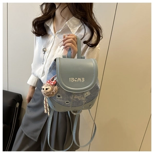 Detail of the blue denim backpack with leather flap and plush doll charm accessory