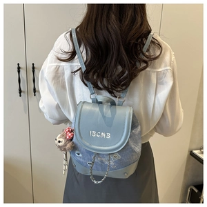 Détail d'un sac à dos en jean bleu clair avec broderie IBCMB et charme en peluche