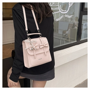 Pink PU leather backpack featuring double bows and pearl heart charm detail on a model