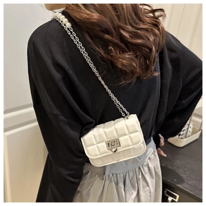 Detail of white quilted mini bag featuring elegant pearl chain strap on model shoulder