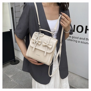 Detail of cream white crossbody bag featuring elegant bows and pearl butterfly charm