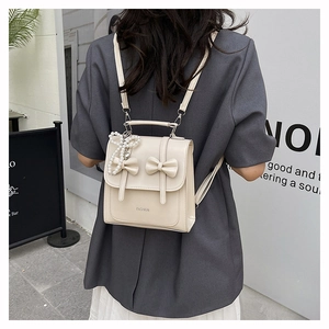 Detail of cream mini backpack featuring 3D bows and a pearl charm in outdoor setting