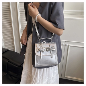 Detail showing the silver metallic leather texture and pearl bow charm on the handbag