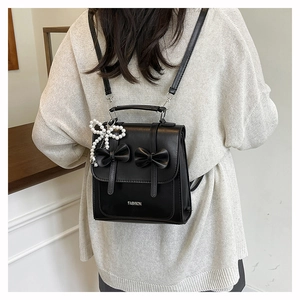 Rear view of a black PU leather backpack with bows and pearl charm on a person