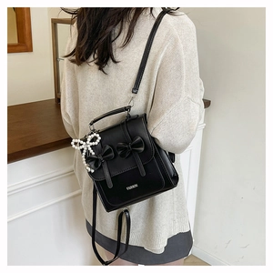 Detail of black PU leather mini backpack with pearl bow charm on a female model