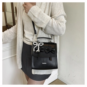 Détail du sac à dos noir à nœud avec breloque en perles et lettrage sur le cuir