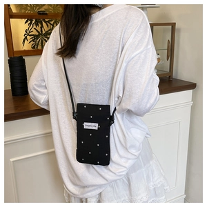Detail view of black canvas crossbody phone bag with star patterns and logo patch