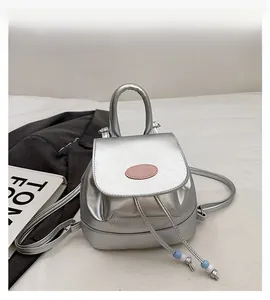 Detail of a silver metallic mini backpack featuring a pink logo plate and drawstring closure