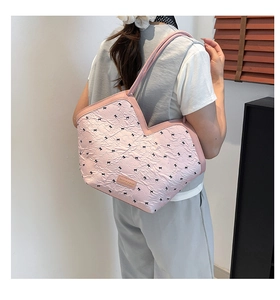 Close-up of pink textured heart-shaped tote bag with black bow print and leather logo plate