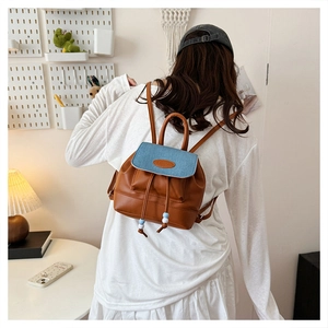 Detail of contrast stitching, blue denim flap and brown leather on mini backpack