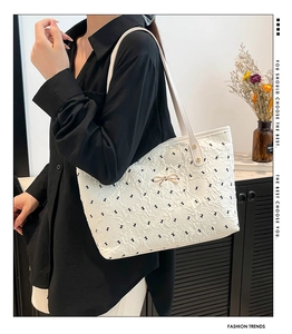 Close-up of quilted white tote bag featuring black bow patterns and gold metal bow hardware