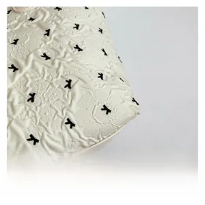 Detail of white wrinkled fabric featuring black embroidered airplane patterns on a bag