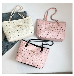 Detail of printed tote bags showing embossed texture and gold bow metal buckle accents