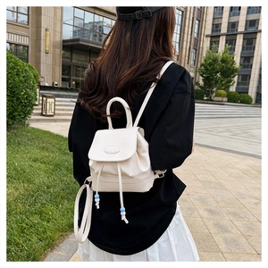 Outdoor shot of cream mini bucket backpack featuring drawstring with decorative blue beads