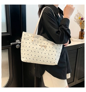 Detail of white tote bag with quilted texture, bow print and rose gold metal bow accent