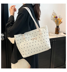 Detail of white tote bag featuring black bow print and gold metallic butterfly buckle
