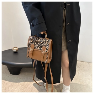 Fashionable leopard print backpack with brown trim held by a model in a black coat