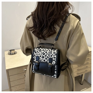 Detail of leopard print mini backpack with dual buckles on a model wearing a beige trench coat