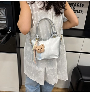 Dettaglio della borsa tote argento metallizzato con ciondolo orso e nastro decorativo
