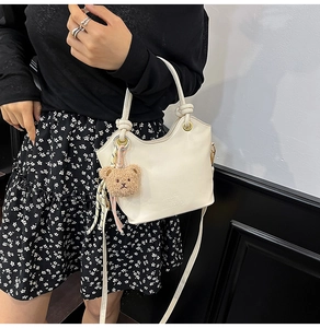 Dettaglio mini borsa a secchiello bianco crema con manico annodato e ciondolo orso