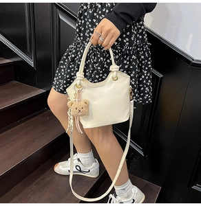 Détail d'un sac seau en cuir PU blanc avec pendentif ours et ruban rayé décoratif