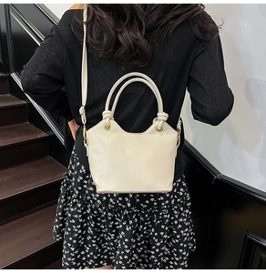 Modella che indossa una borsa a secchiello bianco crema con manici cilindrici e logo
