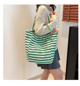 Detail showing green striped canvas tote bag capacity on a woman's shoulder