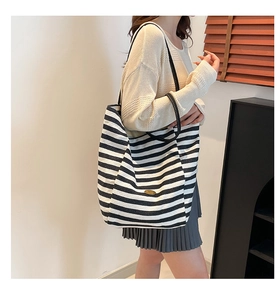 Close-up of black and white striped canvas tote bag with oval metal tag and black strap