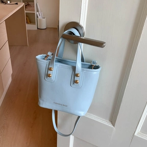 Light blue faux leather mini tote bag with gold studs hanging on a silver door handle