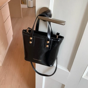 Black glossy PU leather bucket bag with gold rivets and detachable strap on a door handle