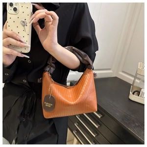 Detail of orange pleated underarm bag with dark brown ruched handle and brand tag