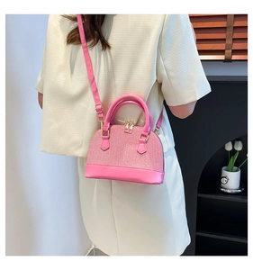 Detail of pink woven shell bag worn by model with adjustable shoulder strap and leather base