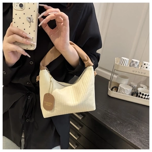Detail view of white pleated handbag with brown scrunchie handle and fashion brand tag
