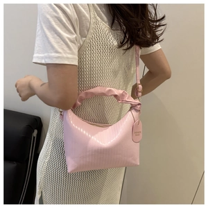 Pink bucket bag with wrinkled handle and textured finish worn by a model in casual style