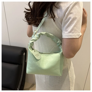 Close-up of mint green textured bucket bag with ruched handle and fashion tag
