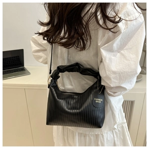 Detail of black cloud bag with pleated handle and vertical texture held by a model