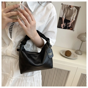 Detail of black pleated texture handbag featuring a fashion bag tag and ruched handle