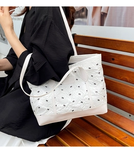 White pleated tote bag with black bow embroidery and double straps on wooden bench
