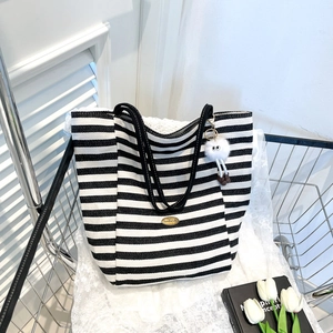 Large black and white striped canvas tote bag with a gold logo and plush charm accessory