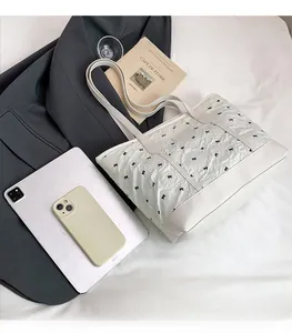 Quilted tote bag with black bows next to an iPad and phone to show large capacity size