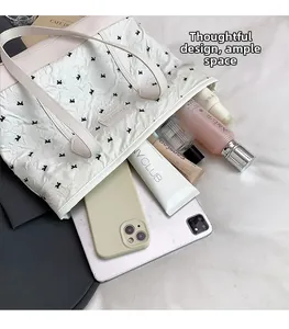 Top-down view of large white tote bag with bow patterns and tech gadgets inside