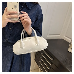 Close-up of white glossy patent leather bowling bag held by a model in denim