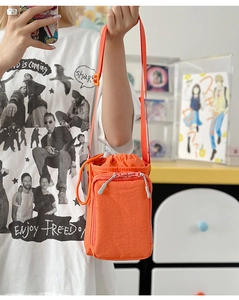 Detail of orange drawstring crossbody bag featuring lightweight nylon texture and front pocket