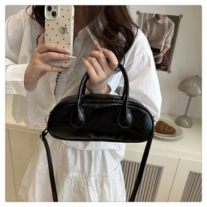 Black glossy oval bowling bag detail with adjustable strap in a minimalist setting