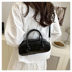 Minimalist black shiny bowling bag with detachable strap shown on a model